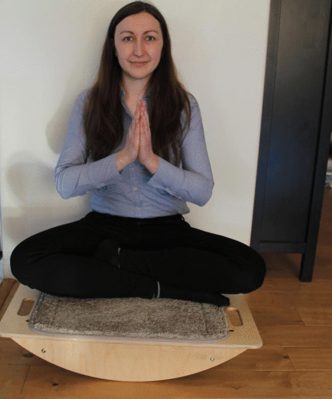 Gif of Sofia sitting on a balance board and moving one hand to the left. As she moves her hand, the weight of her hand gradually tilts the board left as well. This is the mechanism for how hand movements on the number line result in different balance states in Balance Number Line activities.
