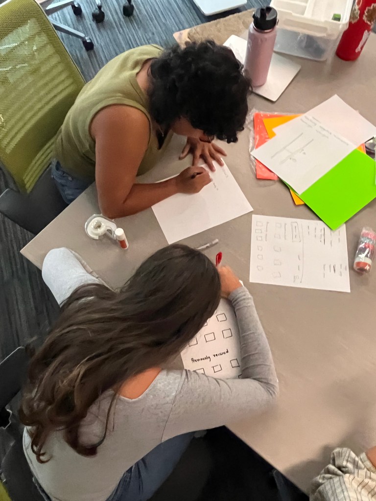 Two co-design day participants work intently on a paper prototype.
