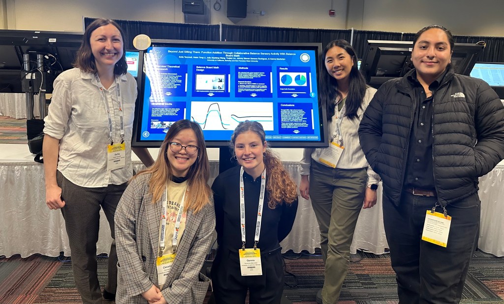 Balance Board Math research team poses smiling in front of a digital poster.