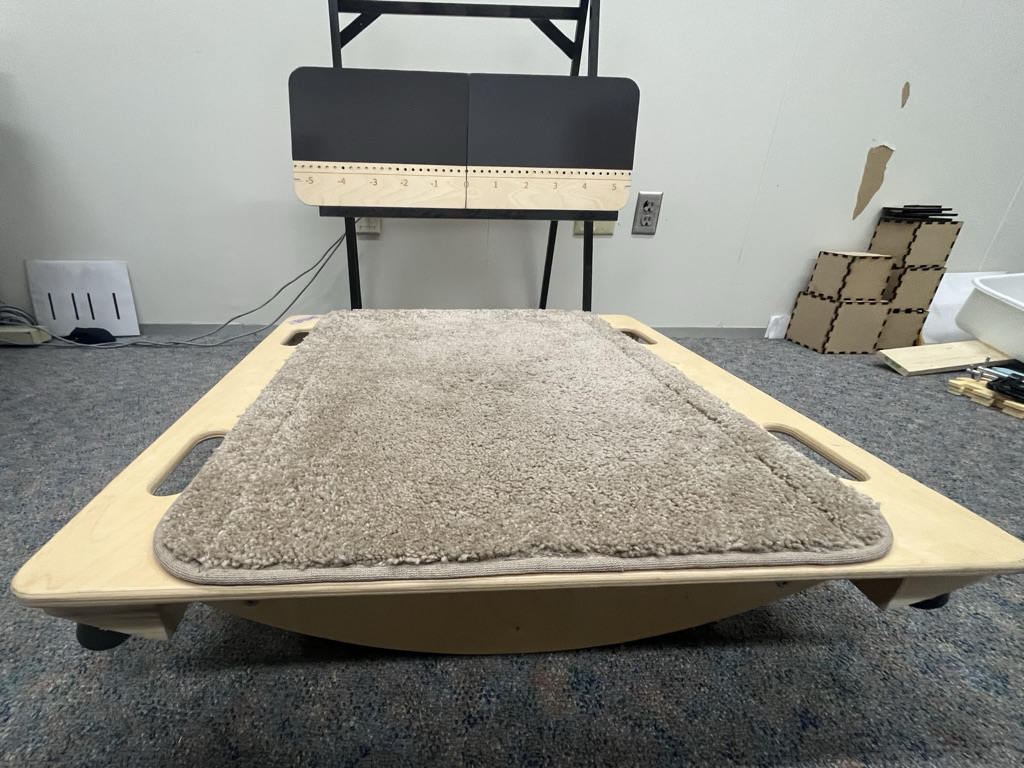 A large flat-topped balance board with a carpet on top in front of a wooden number line with a magnetic surface.