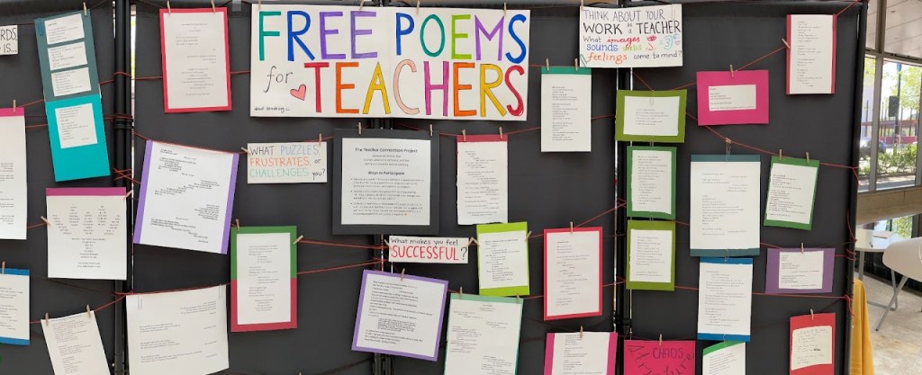 Photograph of a display labelled "FREE POEMS FOR TEACHERS" with about 20 poems hanging from string in front of a black backdrop.